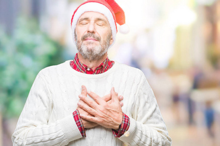 中年老人戴着圣诞帽，在孤立的背景上微笑，双手放在胸前，闭着眼睛，脸上有感激的手势。 健康概念。