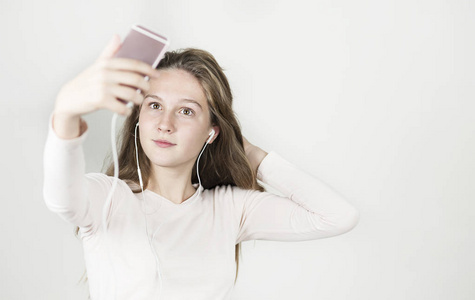 明亮美丽的女孩戴着耳机，手里拿着手机，听音乐，在一个孤立的背景上拍照。
