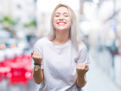 年轻的金发女子在孤立的背景下，非常高兴和兴奋地做着胜利者的手势，举起手臂，微笑着，尖叫着，争取成功。 庆祝概念。