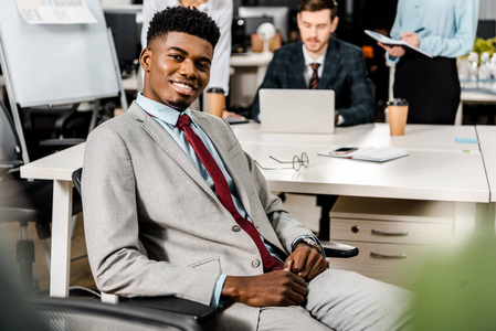 有选择地专注微笑的非裔美国商人和同事在办公室工作的背后