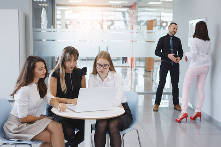 办公室工作人员团队。 商界的女人和男人坐在桌子旁边，拿着笔记本电脑，未来公司的概念。 团队合作。 性别平等。