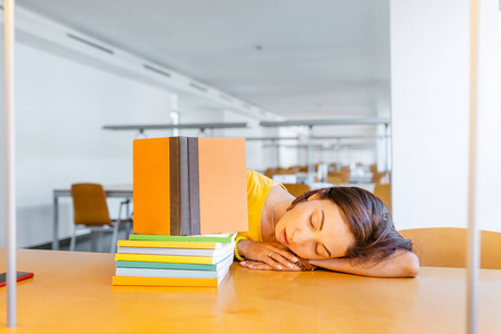 疲惫的学生女孩睡在图书馆的书堆上。 截止日期及考试概念