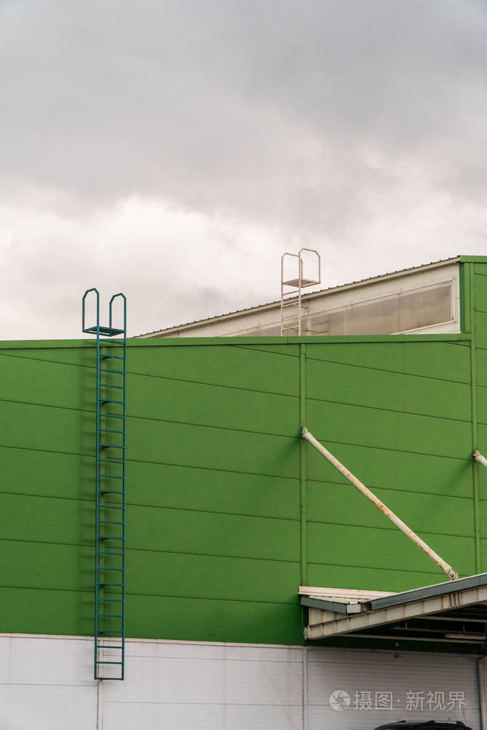一个巨大的仓库的绿色立面,有楼梯,通向暴风雨的天空的屋顶