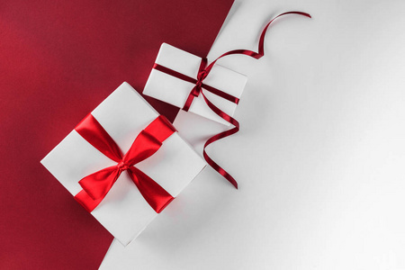 圣诞礼品盒，白色和红色纸背景上有红色丝带装饰。 圣诞节和新年快乐主题。