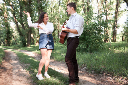 年轻夫妇走在森林里弹吉他跳舞夏天大自然阳光明媚，阳光明媚，绿树成荫，浪漫的感情