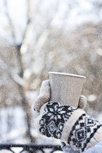 s hands in mittens hold a craft paper glass