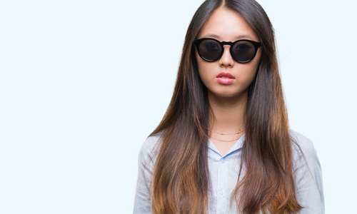 年轻的亚洲女人戴着太阳镜，在孤立的背景上，脸上有着严肃的表情。 简单自然地看着相机。