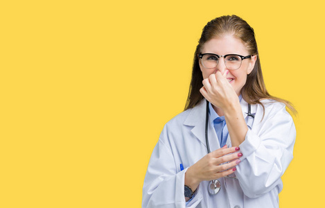 中年成熟的医生女人穿着医用外套，在孤立的背景上闻到一些臭味和令人恶心的难以忍受的气味，用手指在鼻子上屏住呼吸。 难闻的概念。