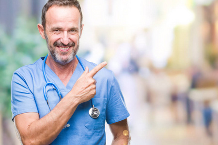 中年老年医生穿着医疗制服，在孤立的背景上欢快地微笑着，用手和手指指向一边，脸上洋溢着快乐和自然的表情，看着相机。