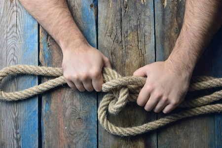 s hands knit rope knot on a wooden background. 