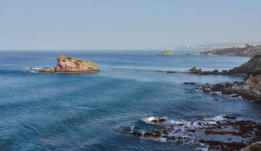 石头和岩石在最前沿，奶油冲浪，潮起潮落，在塞浦路斯的Polis海滩。 背景包含更多的海岸线和地平线上的特洛伊多斯山脉。