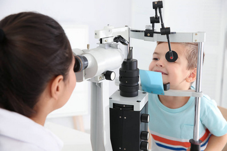 s doctor examining little boy with ophthalmic equipment in clini