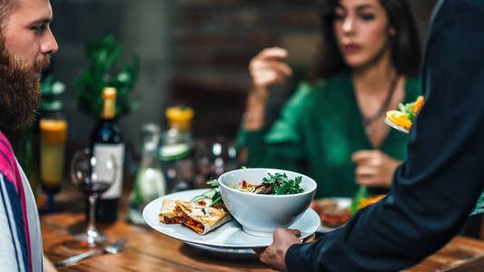一对年轻夫妇在餐厅吃素食晚餐的男性手盘的横向形象。