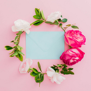 带玫瑰花的花框和粉红色背景上的蓝色信封。 平躺顶部视图。