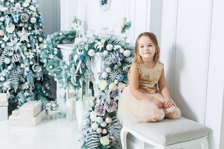 可爱的女孩穿着漂亮的裙子坐在壁炉和圣诞树旁。