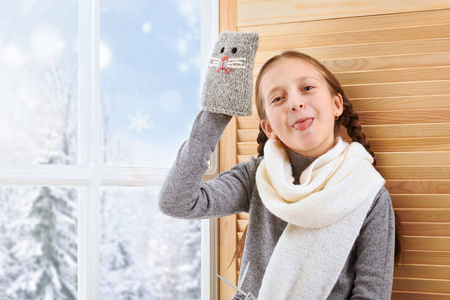 女孩坐在窗台上玩手工手套。 窗外美丽的景色，阳光明媚的冬天和雪。