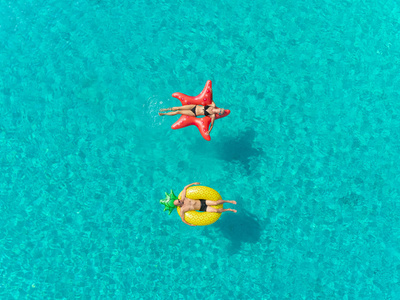 空中近距离观看夫妇漂浮在充气明星和菠萝形状的床垫手。