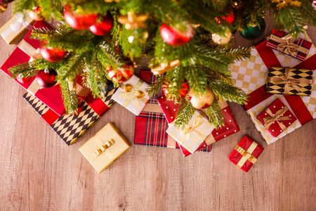 顶部的圣诞树树枝组成与堆叠不同的礼物，在五颜六色的节日包装与蝴蝶结。 木地板上云杉树下的一堆礼物。 背景复制空间。