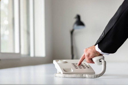 商人用白色的固定电话在白色的办公桌上拨打电话号码。