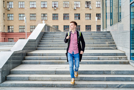 英俊的男学生的全身肖像，背包走下楼梯，在大学校园户外复印空间休息。 教育休息和放松旅行和旅游概念