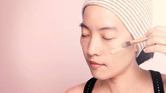 亚洲女孩或妇女，40岁，美丽的脸，日本的外观由粉底液和化妆刷在敏感的皮肤上，帮助她的肤色看起来完美无瑕，真正干瘪。