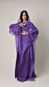 全长肖像的美丽女孩与长发，穿紫色幻想中世纪长袍和斗篷。站在灰色工作室背景上的姿势。