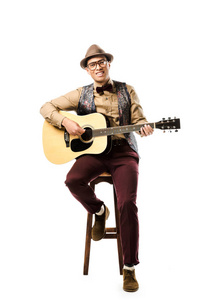 欢快的混血男音乐家戴着帽子戴着眼镜，一边弹着吉他一边坐在白色的椅子上