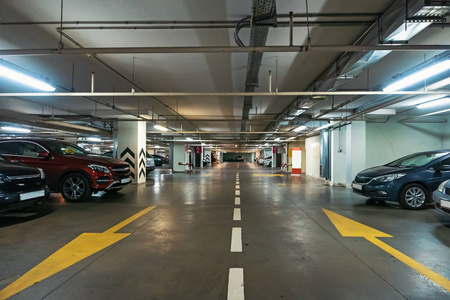 现代购物中心下的照明地下停车场室内有大量的车辆和箭头地板