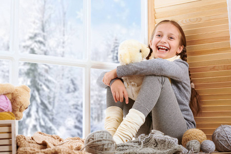 小女孩坐在窗台上玩熊玩具。 窗外美丽的景色，阳光明媚的冬天和雪。