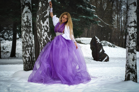 冬天森林里穿着别致的紫丁香裙子的美丽金发女孩