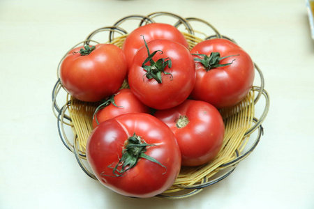 绿枝上的新鲜西红柿在柳条篮子上分离在白色背景上