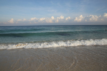 蔚蓝的大海，白色的沙滩上有波浪，天边有云