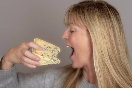 金发女人在吃和享受一块蓝色奶酪