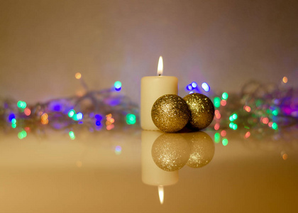 金色圣诞球。 有反光的花环玻璃表面模糊灯光的蜡烛背景