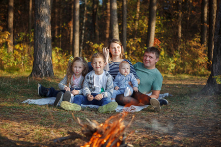 家庭父亲母亲两个男孩和女孩在秋天森林的火边。