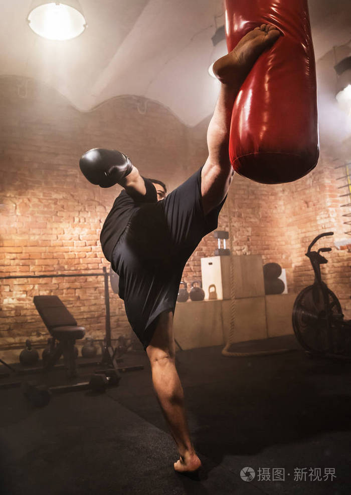 年轻人在训练课上打拳击袋黑暗的工业健身锻炼内部与电影氛围积极的