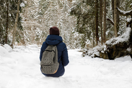 带背包的女孩坐在白雪覆盖的针叶林里。 冬季阴天