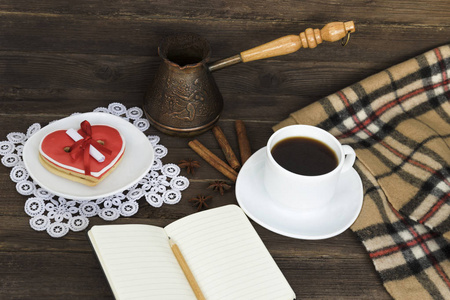 一杯咖啡心形饼干，上面有留言笔记本铅笔和棕色木桌上的咖啡壶。 假期计划。