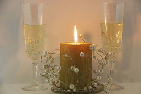 两杯香槟，一支燃烧的金烛，一个白色背景上的花环。