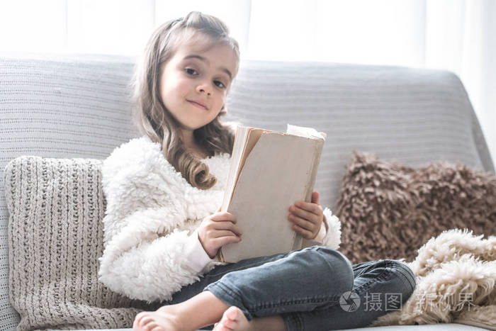 小女孩在舒适的客厅里舒适的沙发上看书,美丽的情感,放松的概念