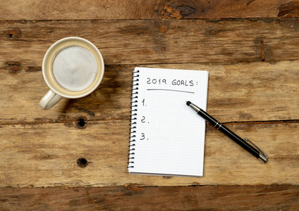 顶部查看2019年新年决议列表，并祝愿新的快乐生活方式在记事本咖啡上的桌子背景下，在愿望列表计划和目标的幸福，灵感和动机的概念。