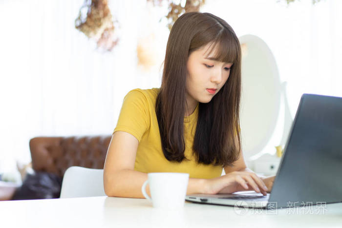 快乐的亚洲美女,在家里的桌子上坐在笔记本电脑上工作