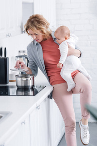 精疲力竭的母亲抱着可爱的婴儿，在厨房做饭
