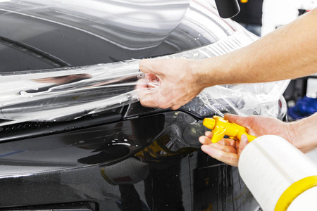 汽车包装专家把乙烯基箔或薄膜放在汽车上。车上的保护膜..用工作工具在汽车上涂上保护膜。汽车细节。透明薄膜。汽车油漆保护。修剪。