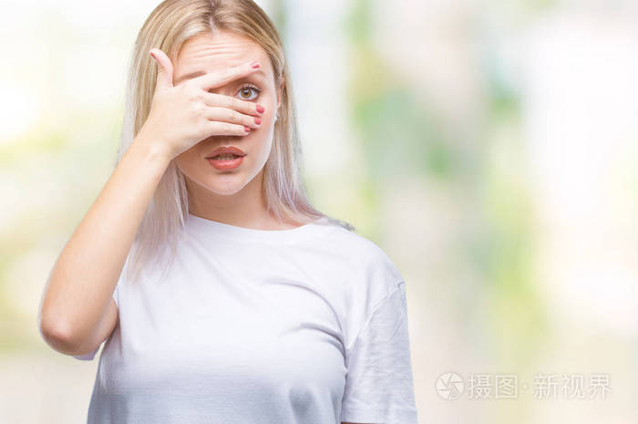 年轻的金发女子在孤立的背景下,震惊地偷看,遮住脸和眼睛,用手透过