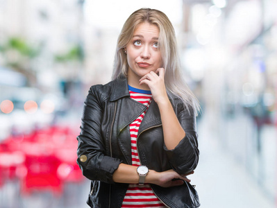 年轻的金发女人穿着黑色夹克，在孤立的背景上，手在下巴上思考问题，沉思的表情。 带着体贴的脸微笑。 怀疑概念。