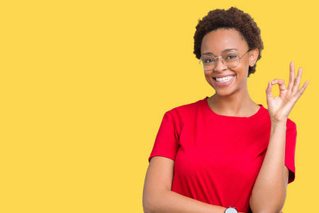 美丽的年轻非洲裔美国妇女戴着眼镜，在孤立的背景上微笑，积极地用手和手指做OK标志。 成功的表达。