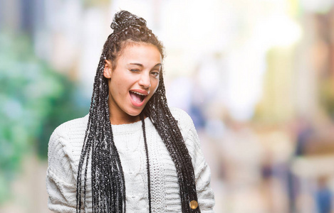 年轻的辫子非洲裔美国女孩穿着毛衣，在孤立的背景下眨眼，看着镜头，的表情，开朗和快乐的脸。
