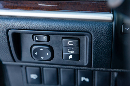 控制汽车内仪表板中央控制台上镜子电动驱动的按钮是现代设计的黑色，有白色的标志和符号。