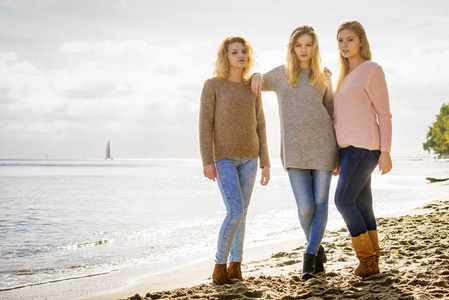 在温暖的秋日天气里，三个穿毛衣的时髦女人把空闲时间花在阳光明媚的海滩上。时尚模特户外模特